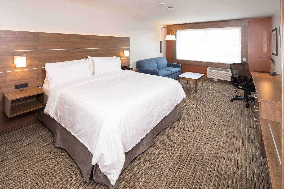 A hotel room with a large bed, a desk, a chair, and a sofa.