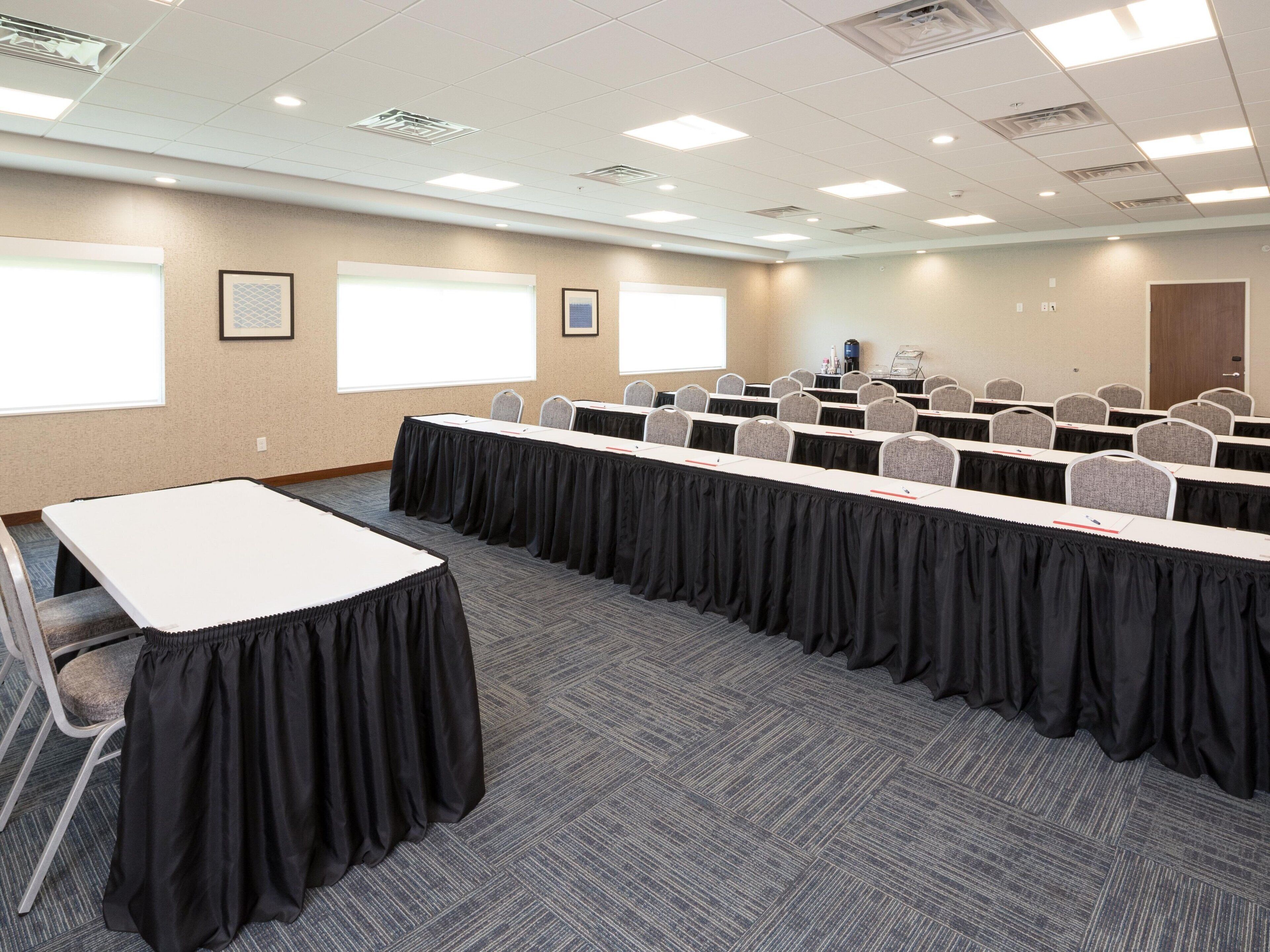 A conference room with multiple tables and chairs, carpeted flooring, and large windows. - Holiday Inn Express and Suites Kalamazoo West by IHG (Kalamazoo)