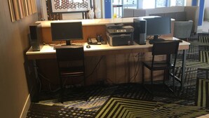 Een werkruimte met twee bureaus, stoelen, een printer en een kamerkleed met een patroon.