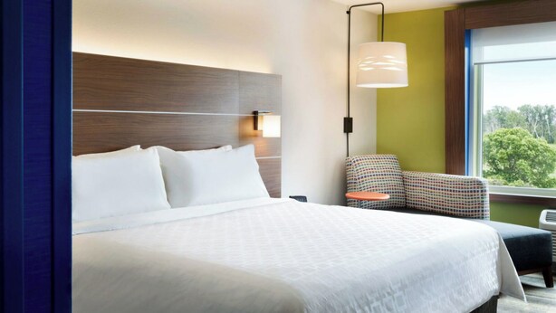 Hotelkamer met een groot bed, nachtkastje, stoel en raam met uitzicht op bomen.