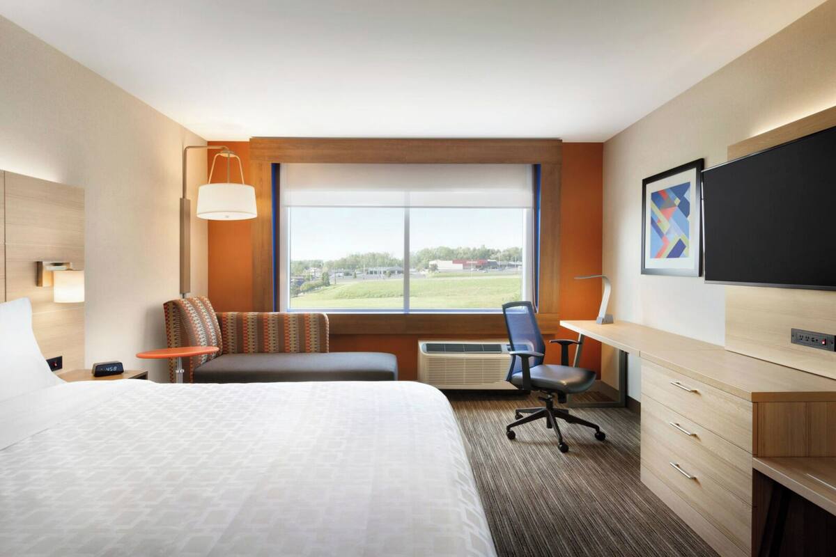 A hotel room with a large bed, a desk, a chair, a TV, and a window with a view of the outdoors.