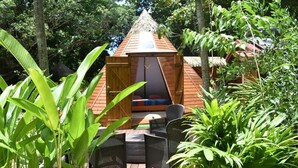 Een houten hut met rieten dak, omringd door weelderige begroeiing.