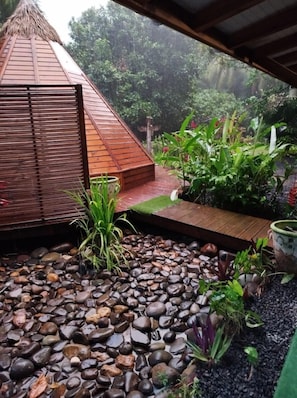 A garden with a wooden deck, a thatched-roof structure, and a variety of plants.
