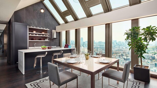 Una cocina moderna con vistas a la ciudad, un comedor con mesa puesta para cuatro personas, y una planta grande en maceta.