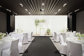 Un salón de banquetes con mesas redondas, sillas blancas y una decoración floral en el centro.