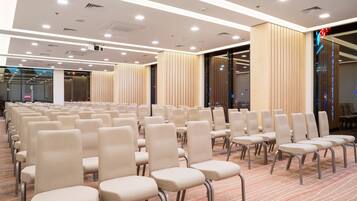 A conference room with rows of beige chairs, a carpeted floor, and a modern ceiling with recessed lighting.