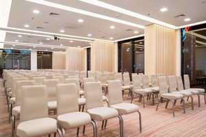 A conference room with rows of beige chairs, a carpeted floor, and a modern ceiling with recessed lighting.