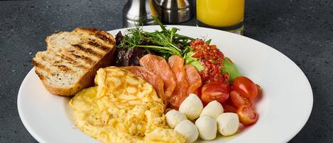 Un plato de comida para el desayuno con tostadas, huevos revueltos, salmón ahumado, tomates, bolitas de mozzarella y vegetales verdes.