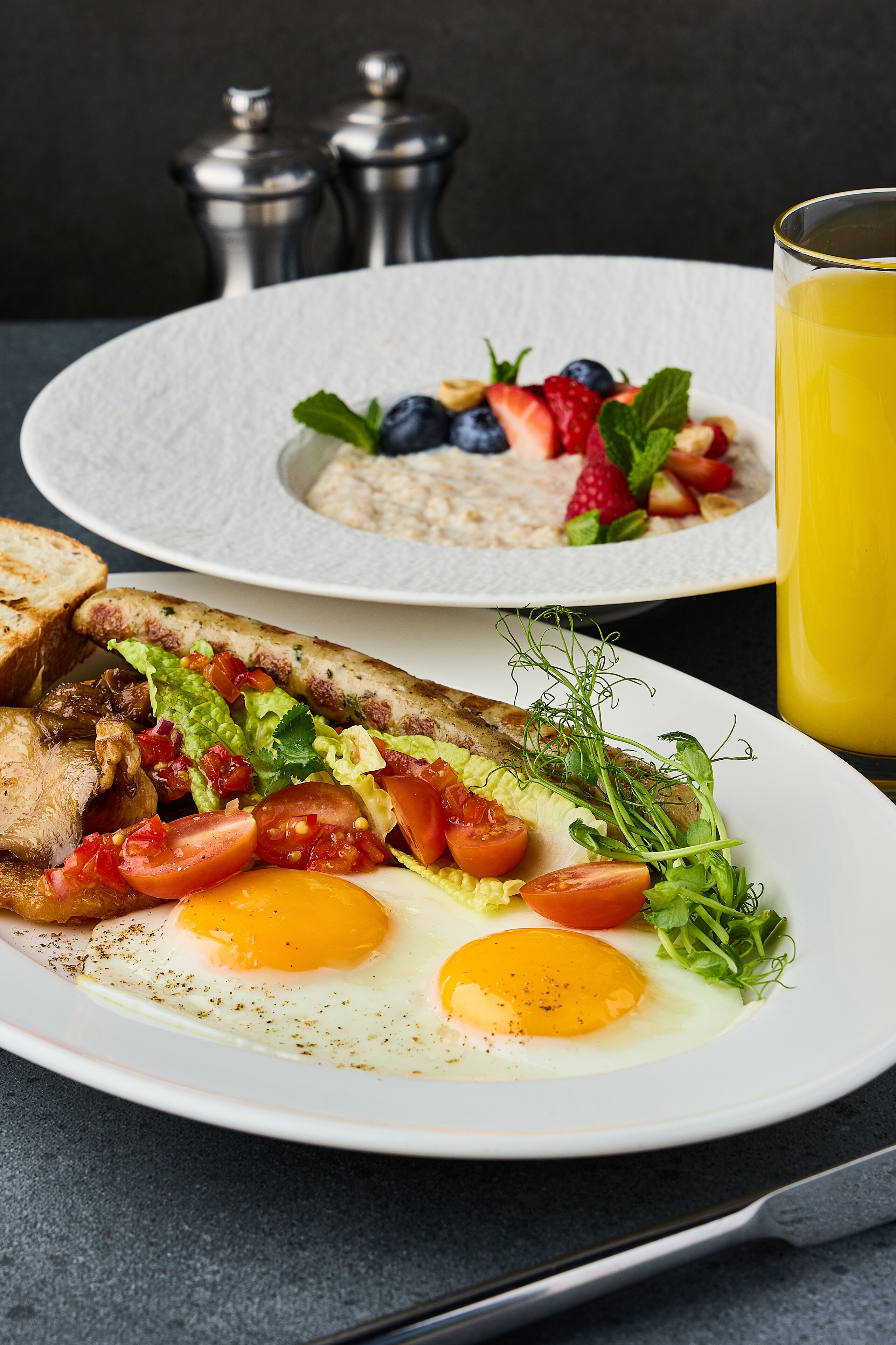 Een ontbijttafel met twee borden eten, één met eieren en groenten, en de ander met toast en fruit.