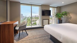 A modern hotel room with a large bed, a desk, a chair, a television mounted on the wall, and a large window offering a city view. - Sky Loft Hotel by Rixwell (Kyiv)