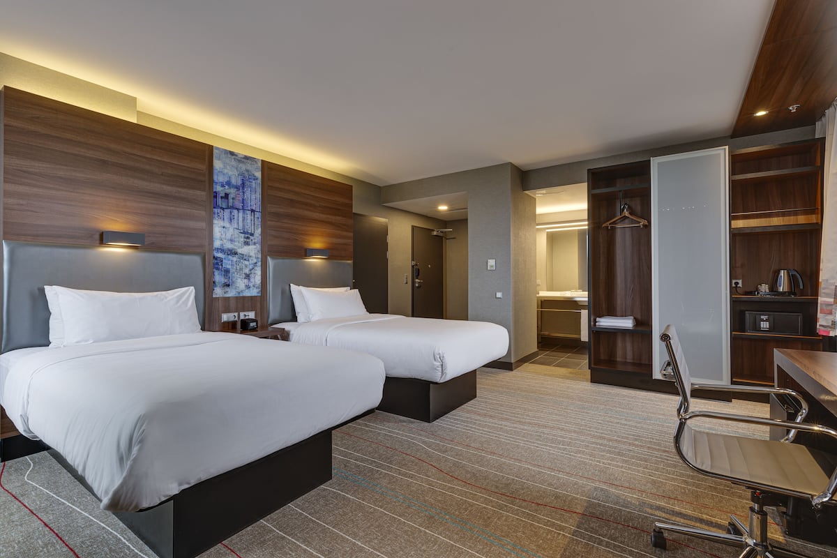 Habitación de hotel con dos camas, un escritorio, una silla y un armario.