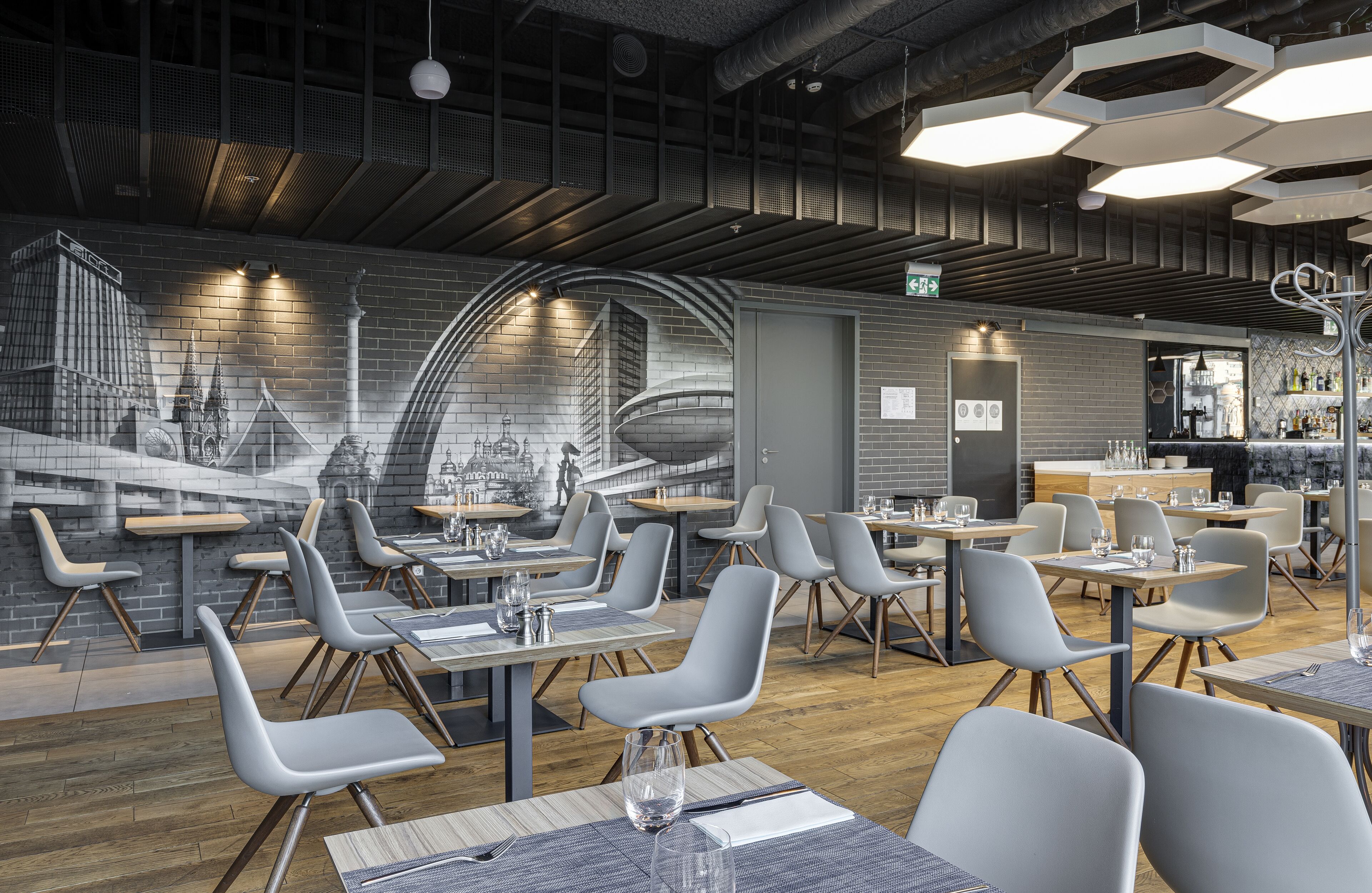A modern restaurant interior with high tables and chairs, a brick wall mural, and a bar area.