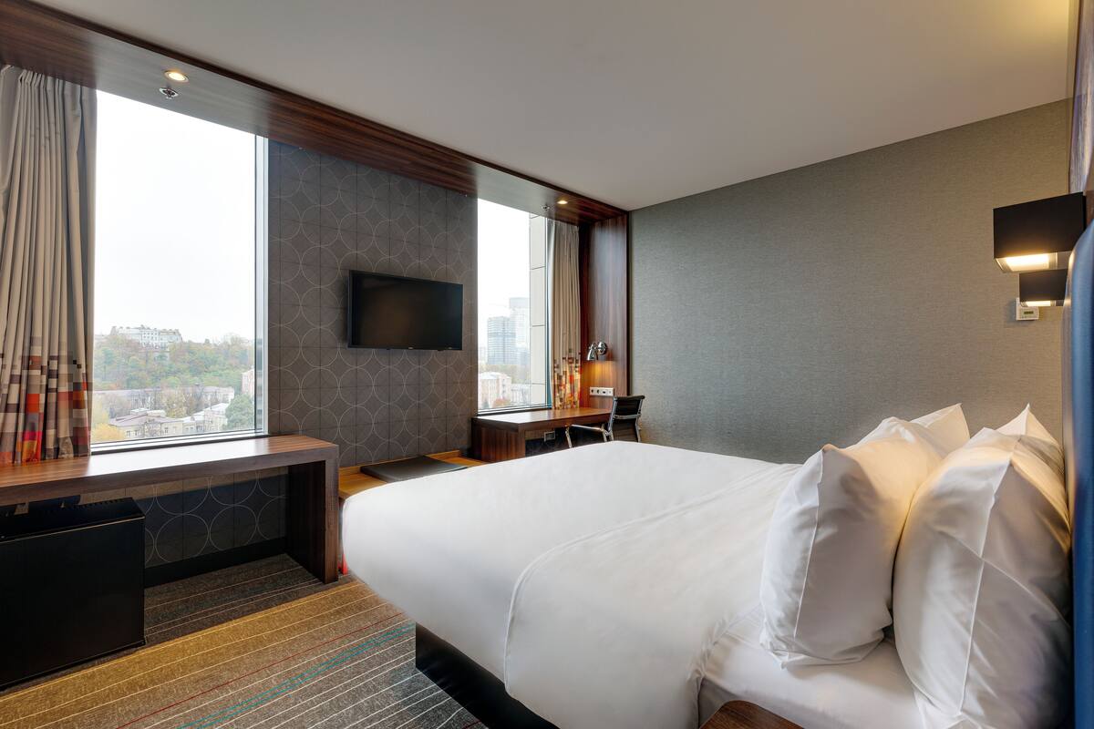 Una habitación de hotel con una cama grande, un escritorio, un televisor de pantalla plana y vistas a la ciudad.