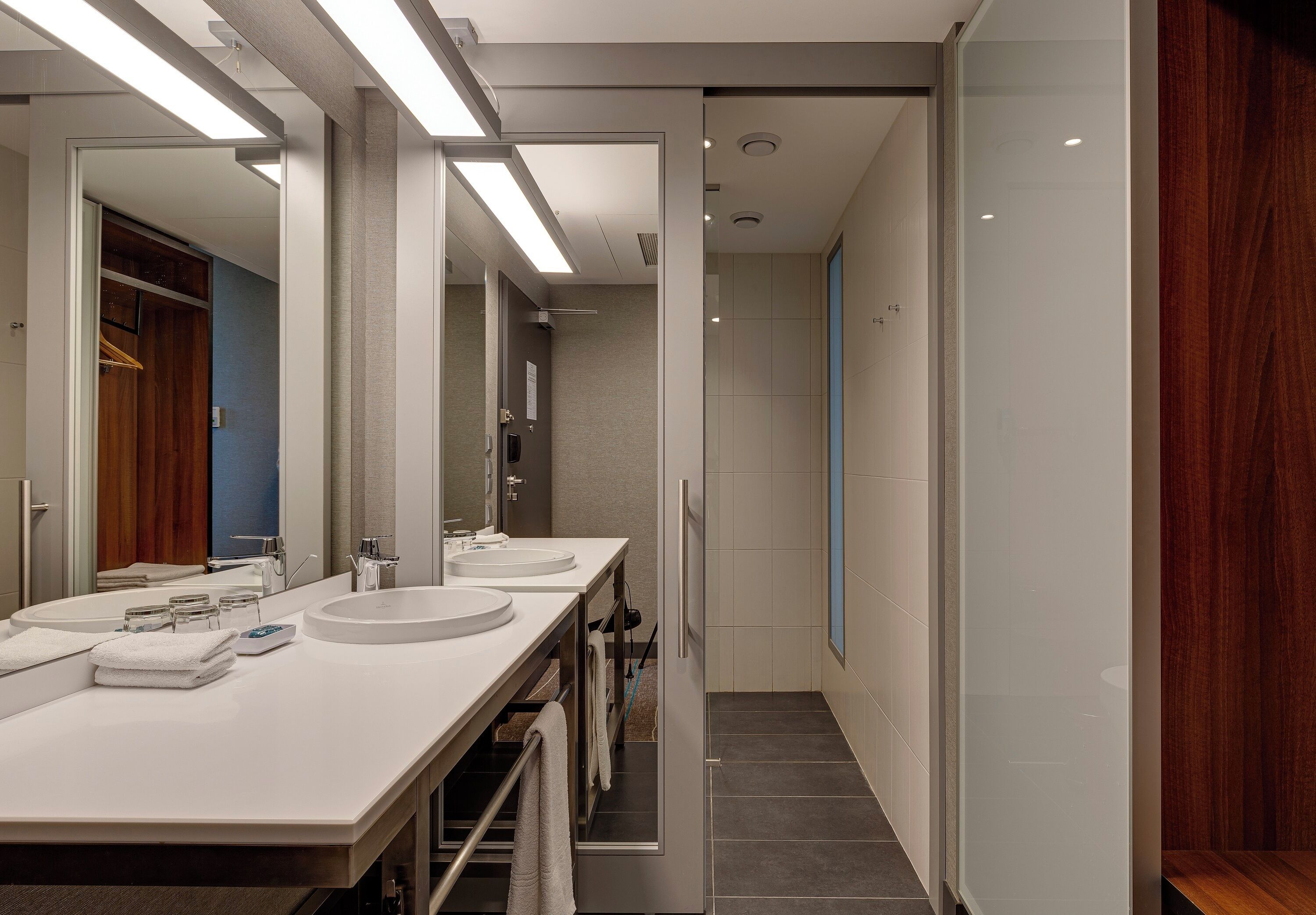 A modern bathroom with two sinks, a mirror, and a towel rack.