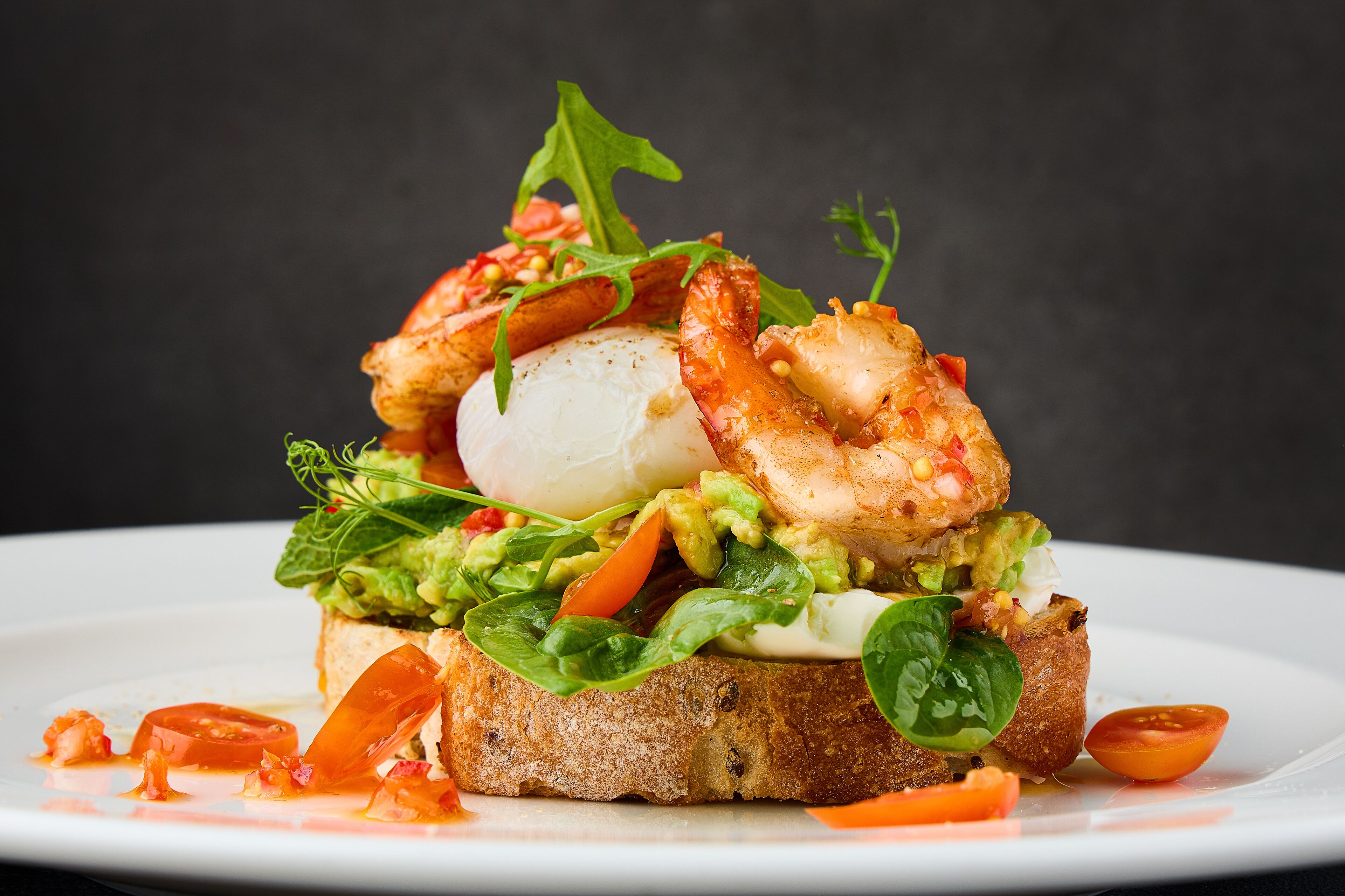 Een sandwich met avocado, tomaat en bladgroenten op een sneetje brood.