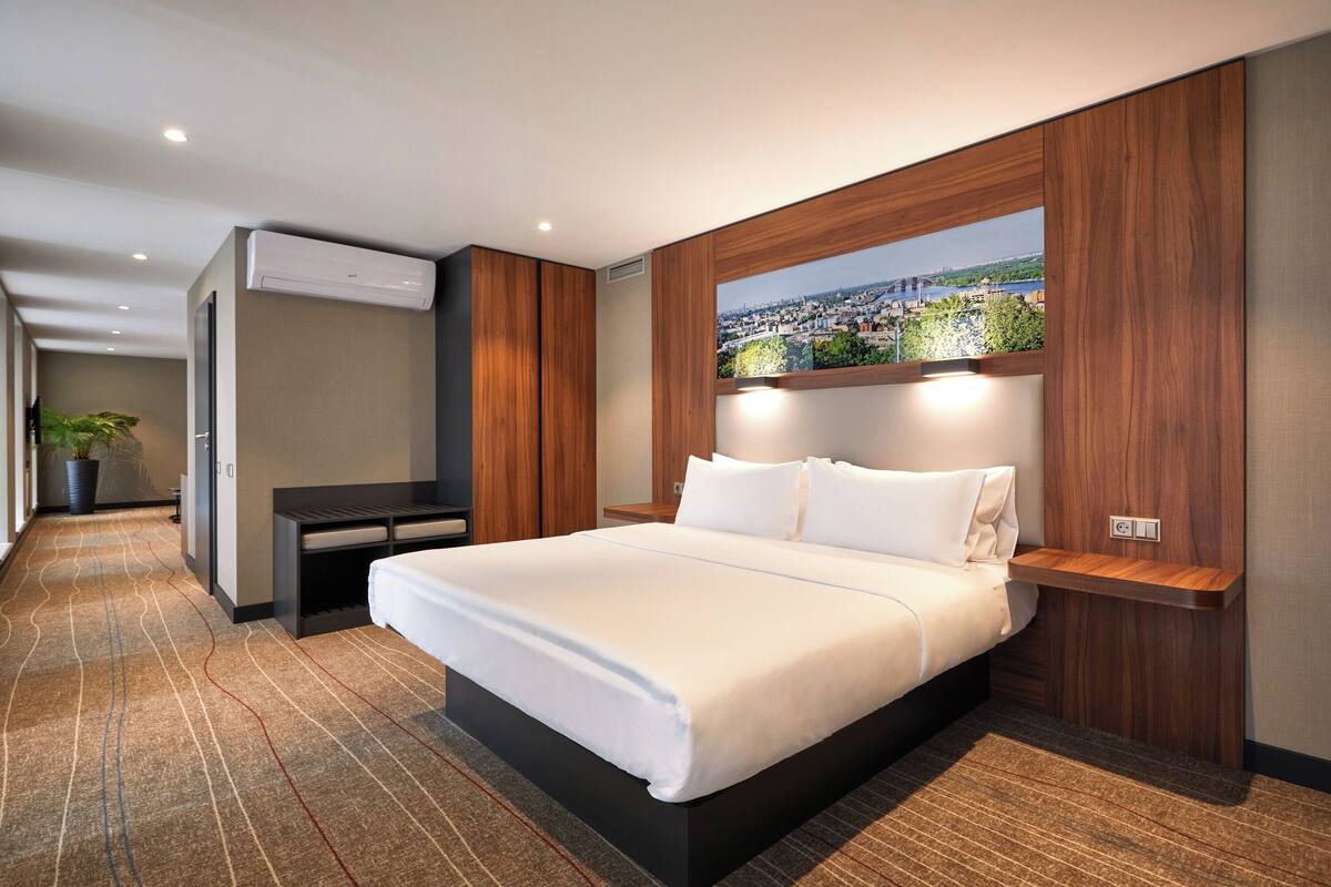 Una habitación de hotel moderna con una cama grande, vista a la ciudad a través de una ventana y un escritorio empotrado con silla.