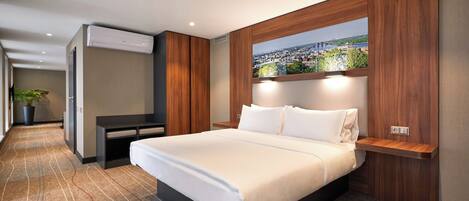 Una habitación de hotel moderna con una cama grande, vista a la ciudad a través de una ventana y un escritorio empotrado con silla.