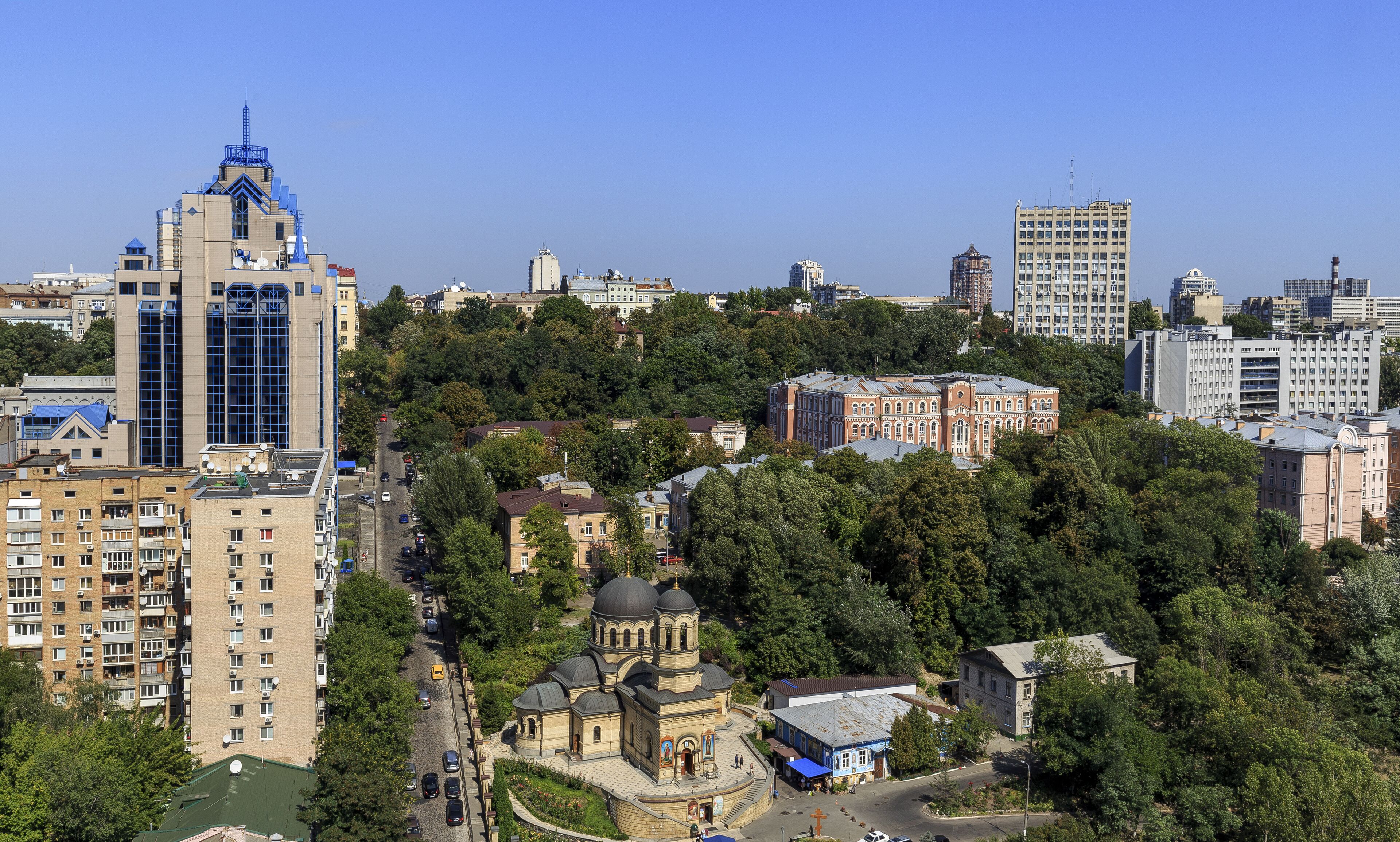 A cityscape with a mix of modern and historic buildings, including a prominent tower and a church with domes.