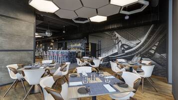 Un restaurant moderne avec des luminaires hexagonaux au plafond, des chaises blanches et marron, et une fresque murale.