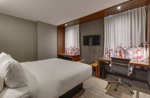Een hotelkamer met een groot bed, een bureau, een stoel, een aan de muur bevestigde televisie en een raam met gordijnen.