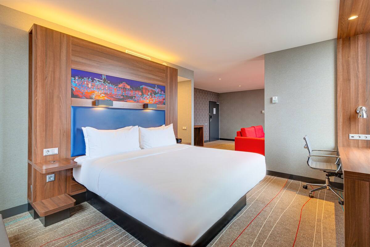 Una habitación de hotel con una cama grande, un escritorio, una silla y un cuadro en la pared.