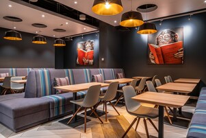A modern restaurant with a mix of seating options including a sofa and tables, overhead lighting, and artwork on the walls.