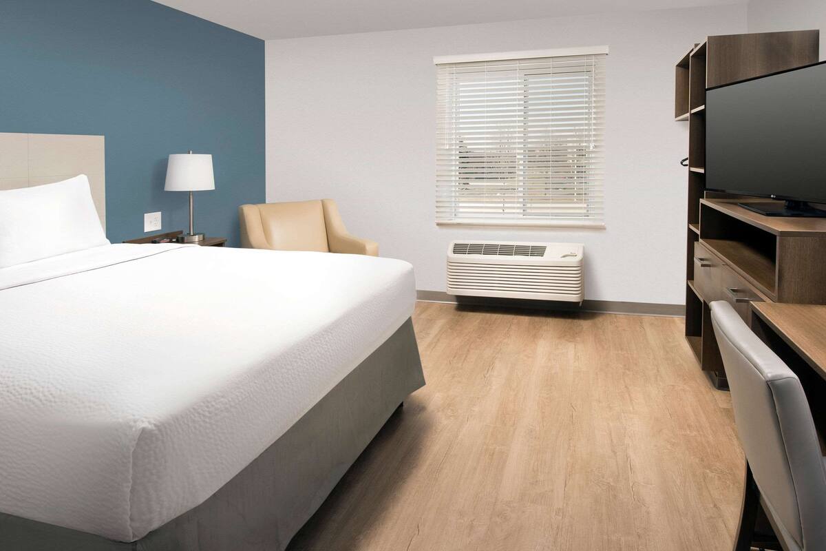 A hotel room with a bed, a chair, a TV, and a window with blinds.