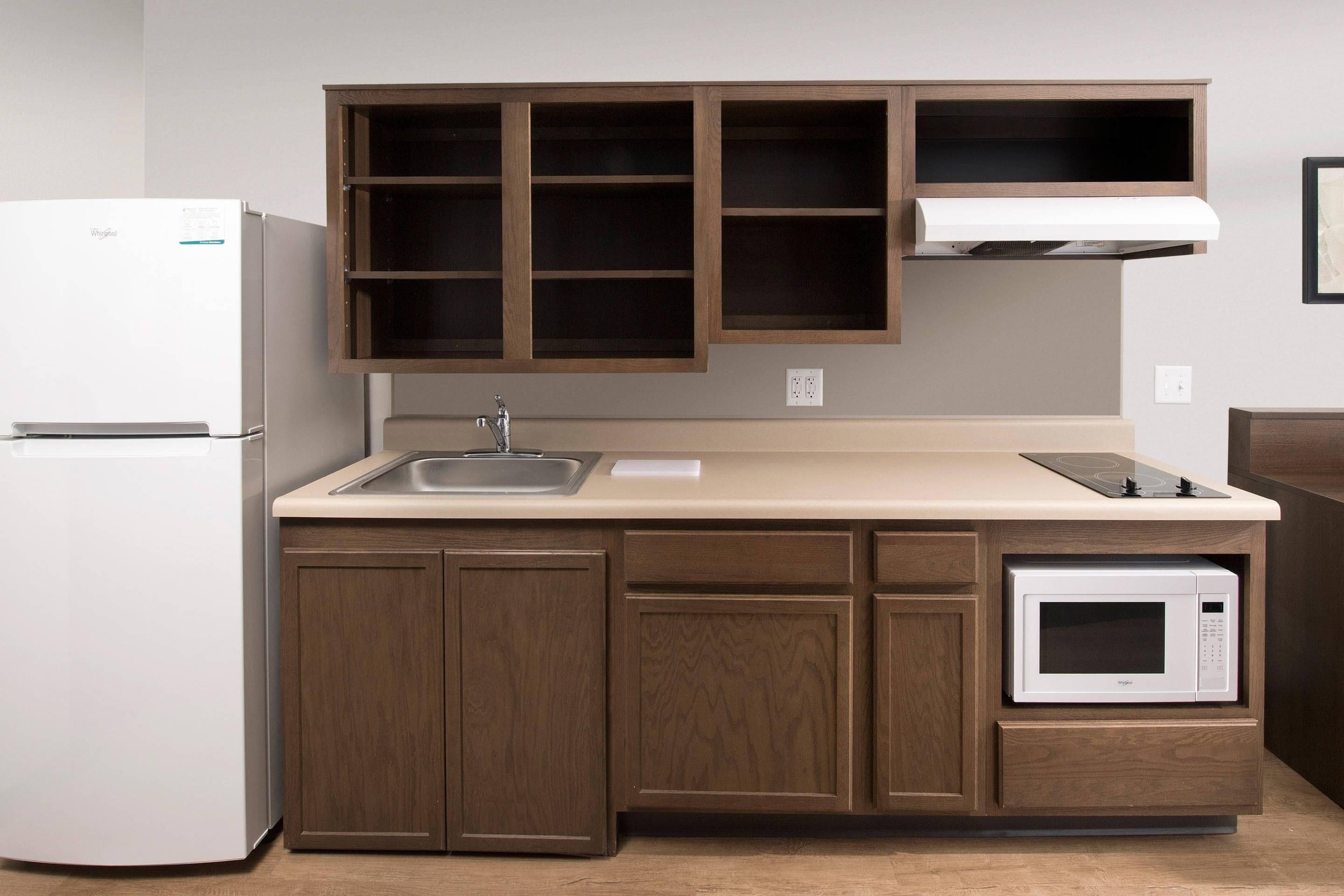 A kitchen with a refrigerator, a microwave, a sink, and wooden cabinets.