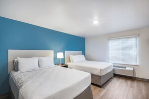 Habitación de hotel con dos camas, una pared de acento azul, una ventana con persianas y un calentador empotrado.