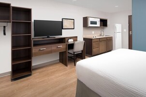 Habitación de hotel con cama, escritorio con silla, armario, televisor, microondas y lavamanos.