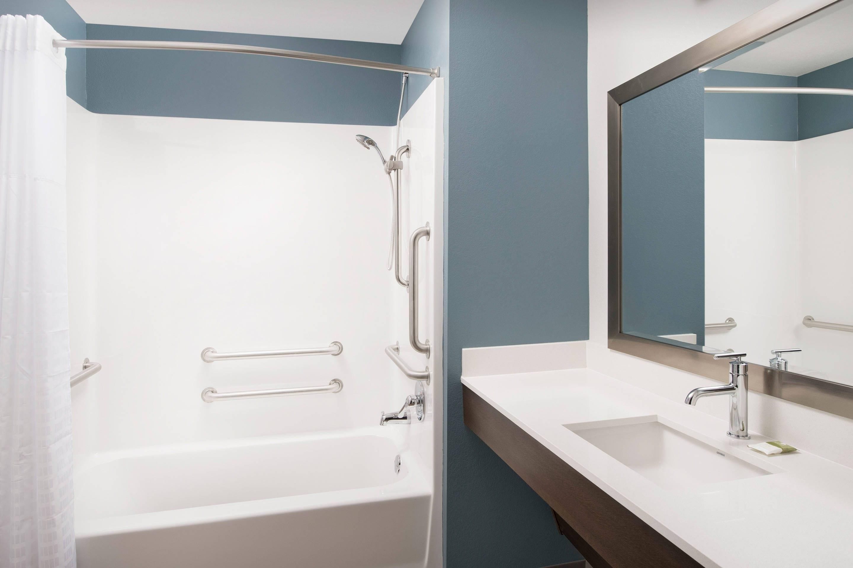 A bathroom with a bathtub, two sinks, a mirror, and grab bars.