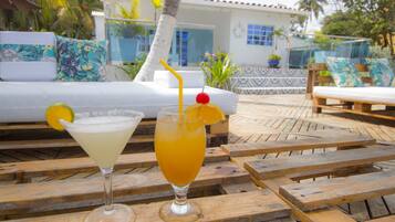 Una mesa de madera con dos bebidas, un sofá blanco y un patio con baldosas y palmeras al fondo.
