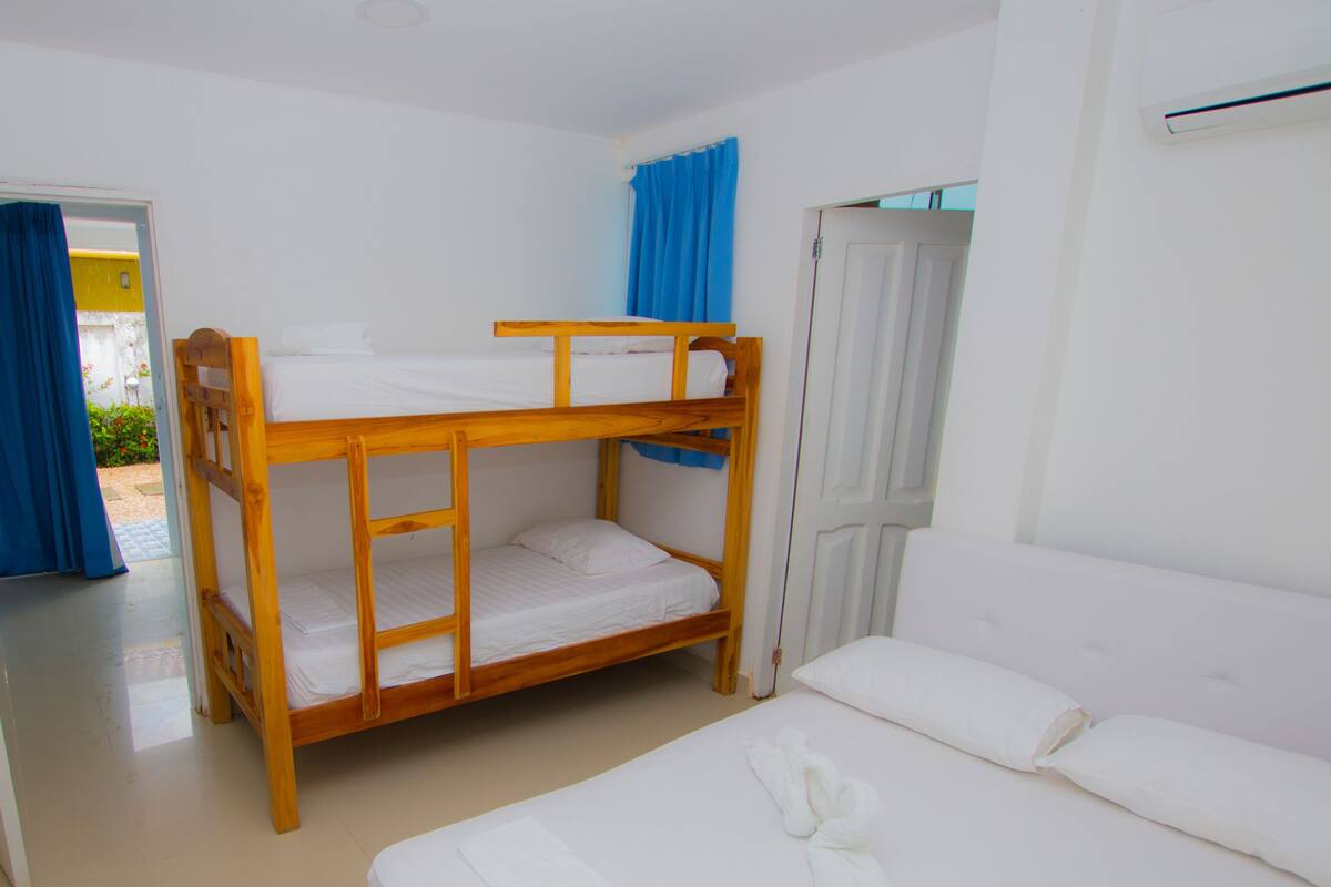 Een kamer met stapelbedden en een eenpersoonsbed, een deur en een raam met blauwe gordijnen.