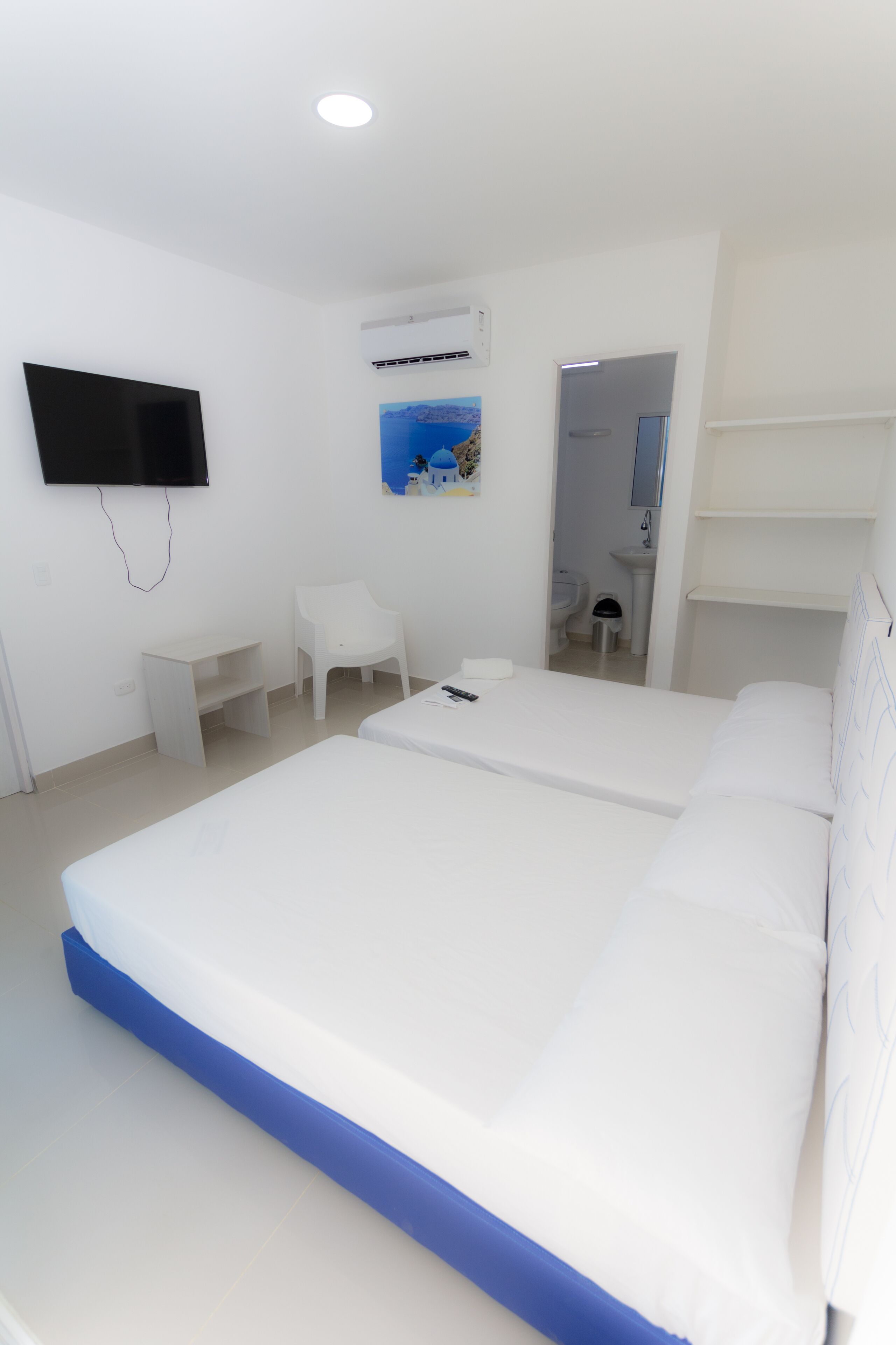 A modern hotel room with a large bed, a desk, a chair, a TV, and a bathroom visible through an open door.