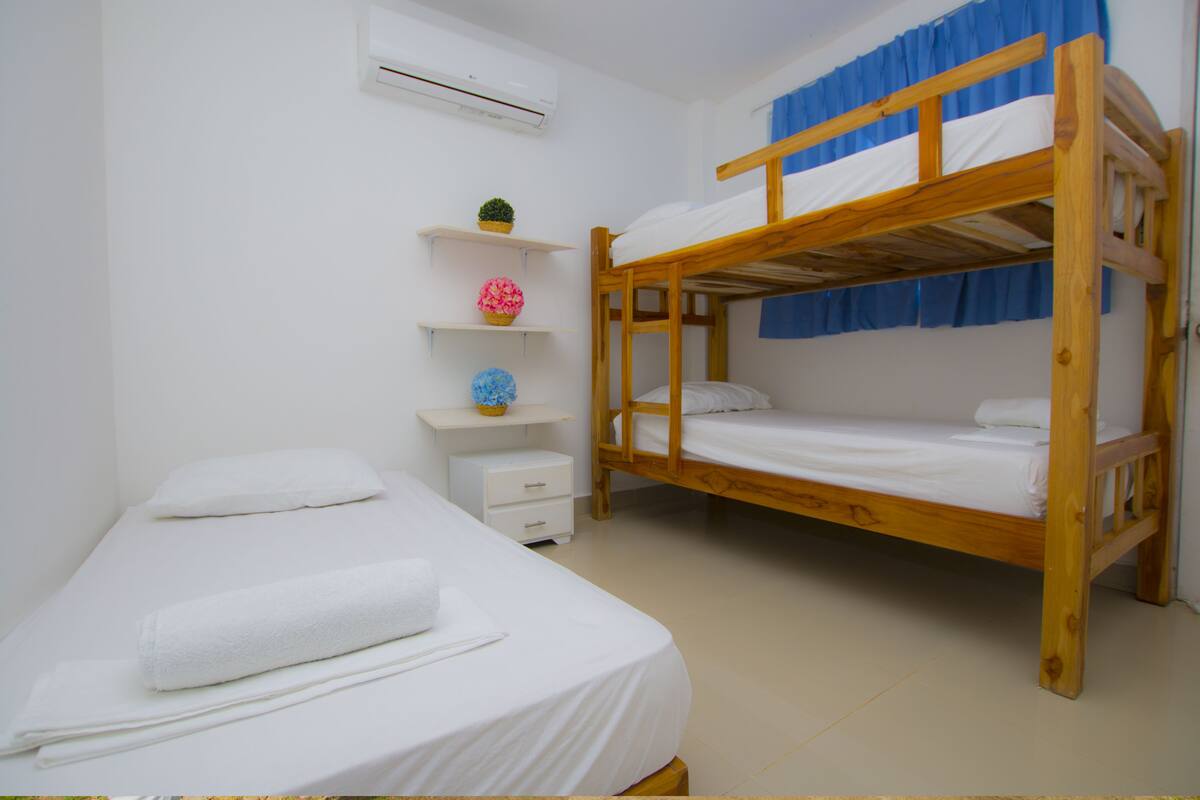 Een kamer met een stapelbed, een enkel bed, een kleine witte dressoir en planken met decoratieve spullen.