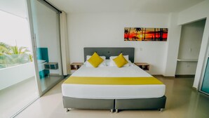 Quarto de hotel moderno com uma cama grande, uma pintura de pôr do sol e uma varanda com plantas.