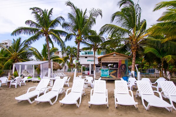 A beach with white lounge chairs, palm trees, and a small building with a sign.