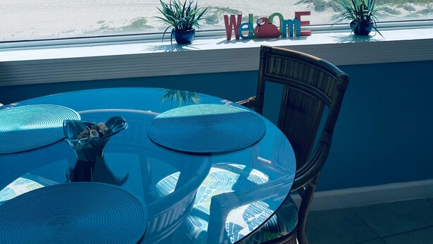 Une vue depuis une fenêtre donnant sur une plage, avec une pancarte indiquant « Bienvenue » et une autre pancarte indiquant « Direction la plage ! ».