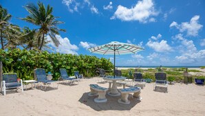 Une terrasse au bord de la plage, avec des chaises longues, une table et un parasol.