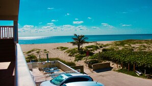 Un balcon donnant sur une plage, une voiture garée et quelques chaises longues.