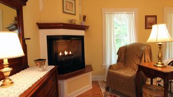 A cozy living room with a fireplace, a comfortable armchair, and a wooden side table with a lamp.