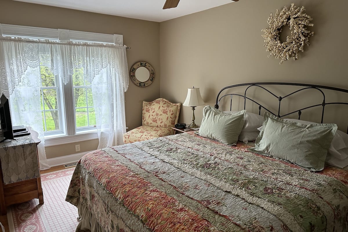 A bedroom with a bed, a chair, a desk, a lamp, and a window with curtains.