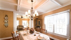 A dining room with a chandelier, a table set for four, and a view of the outdoors through large windows. - Maple Shade Bed & Breakfast  (Stillwater)