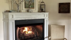 A fireplace with a fire, a white mantelpiece, a vase with branches, and a framed picture on the wall. - Maple Shade Bed & Breakfast  (Stillwater)