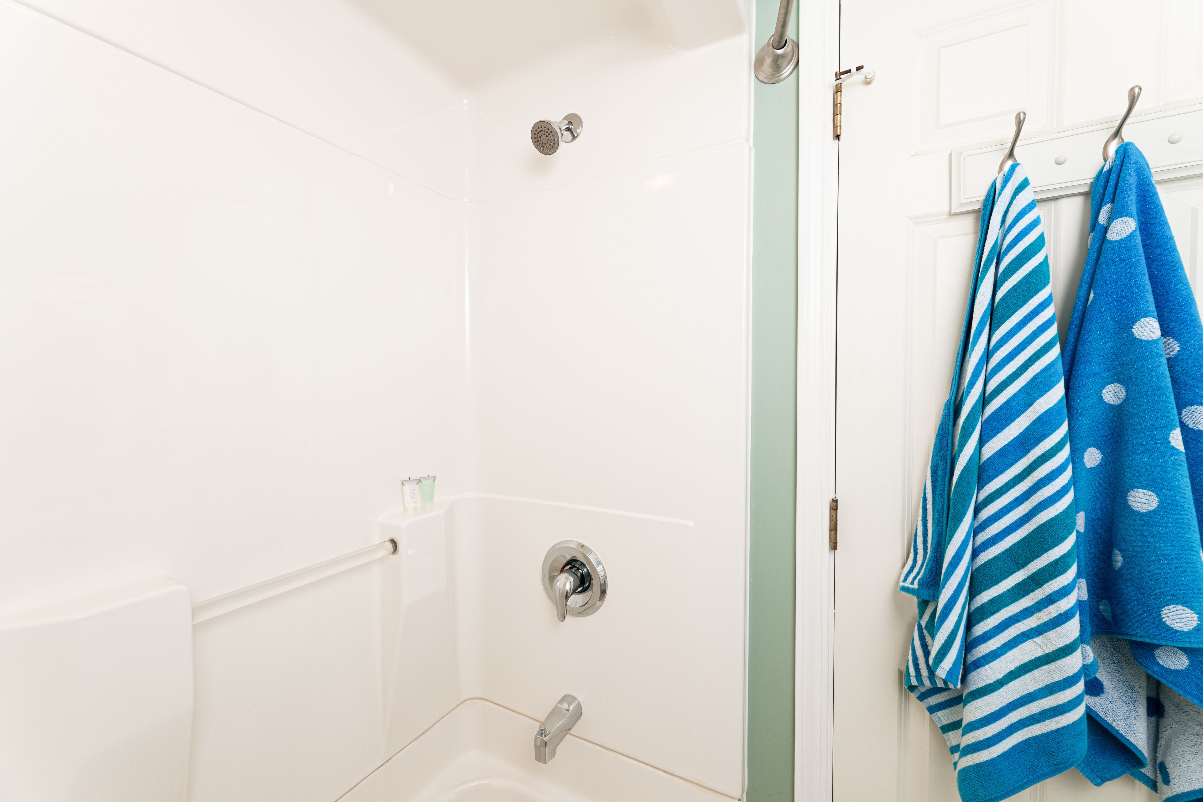 Un'area doccia con porta in vetro, una vasca da bagno bianca e un portascope con asciugamani blu.