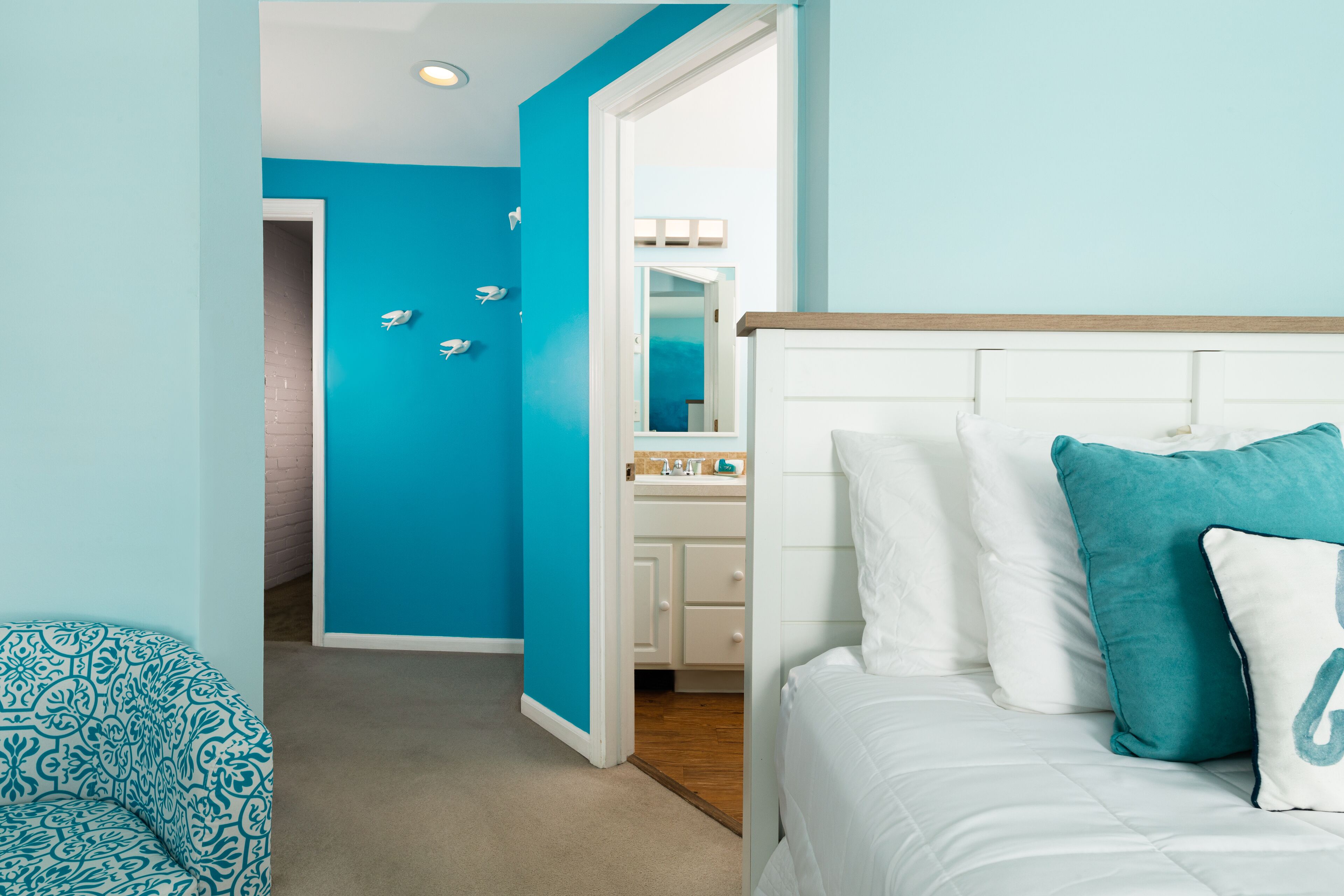 Un dormitorio con cama, mesita de noche y baño visible a través de una puerta abierta.