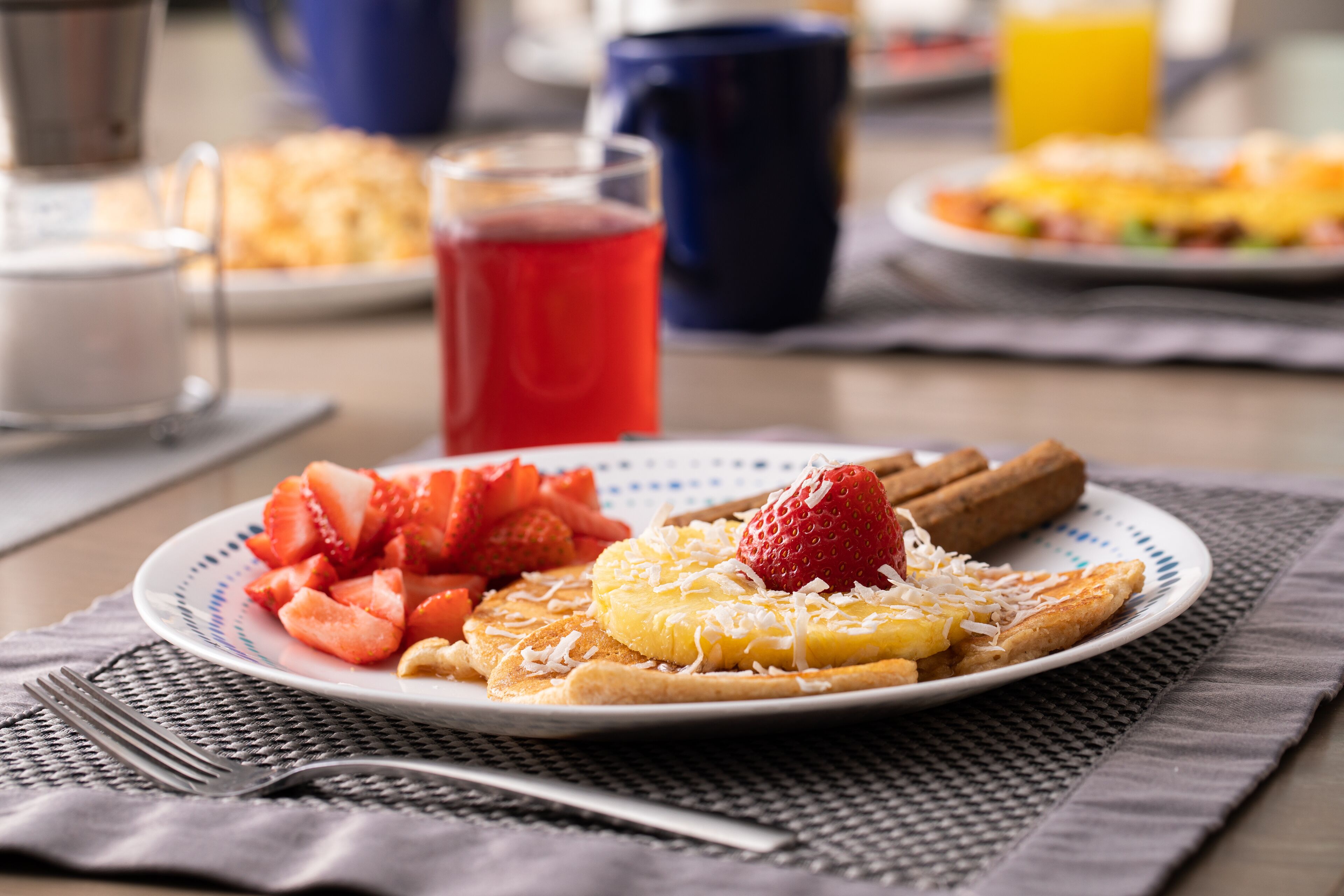 A breakfast plate with strawberries, a slice of pineapple, and a strawberry on toast, accompanied by a glass of red juice.