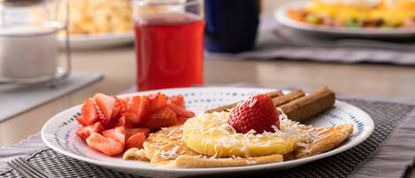 A breakfast plate with strawberries, a slice of pineapple, and a strawberry on toast, accompanied by a glass of red juice.