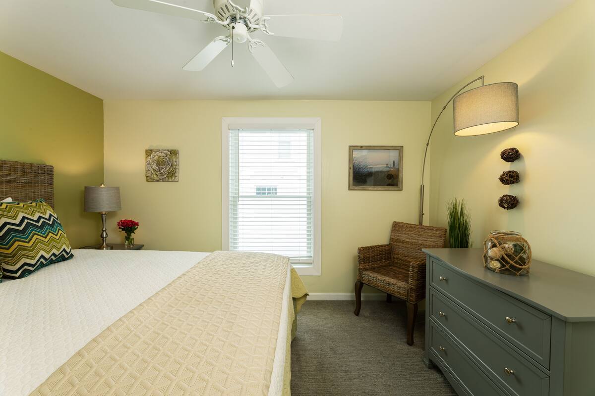 A bedroom with a bed, a chair, a dresser, a lamp, and a ceiling fan.