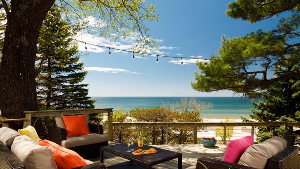 An outdoor seating area with wicker furniture, a table with a bottle and glasses, and a view of the ocean. - Looking Glass Beachfront Inn (Grand Haven)